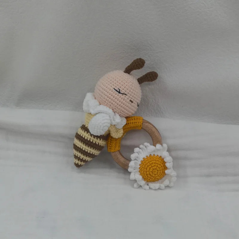 A handcrafted wooden baby rattle and teether ring shaped like a bee with a white beard and a flower.