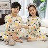 Two children wearing matching light beige cotton pajamas with an astronaut print and flower headband.
