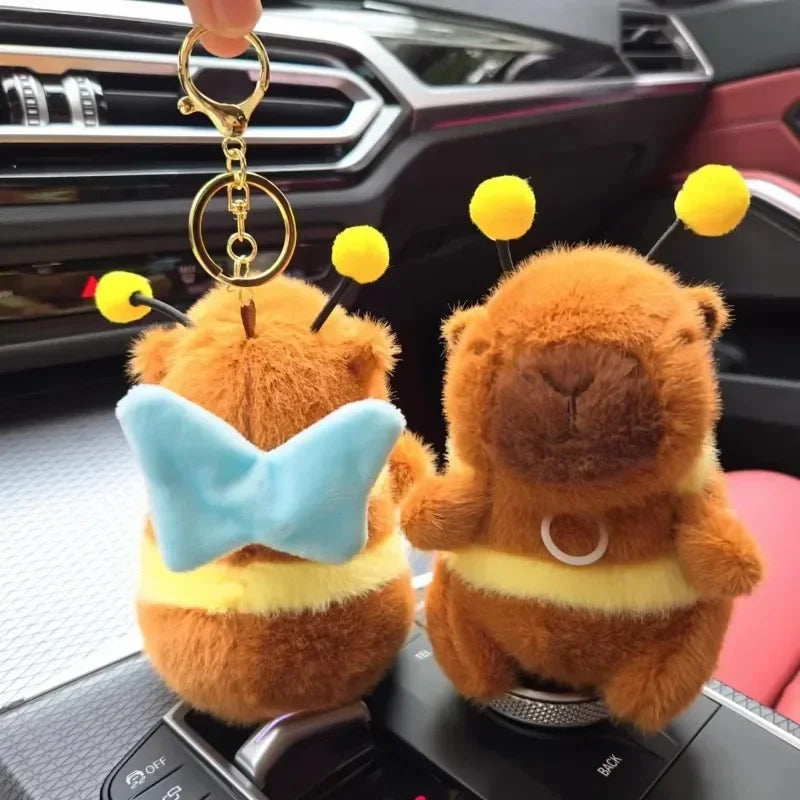 A fluffy orange capybara plush toy with blue wings and a gold keychain attached to it.