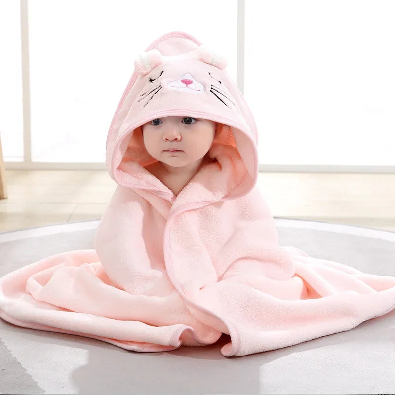 A baby wearing a pink hooded towel resembling a cat is shown lying down.