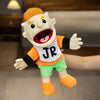 A realistic plush hand puppet with blonde hair and an orange shirt and green shorts is shown against a blurred background.
