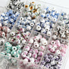 A clear plastic container filled with small round ceramic flower beads in various blue, white, and pink colors for jewelry ma