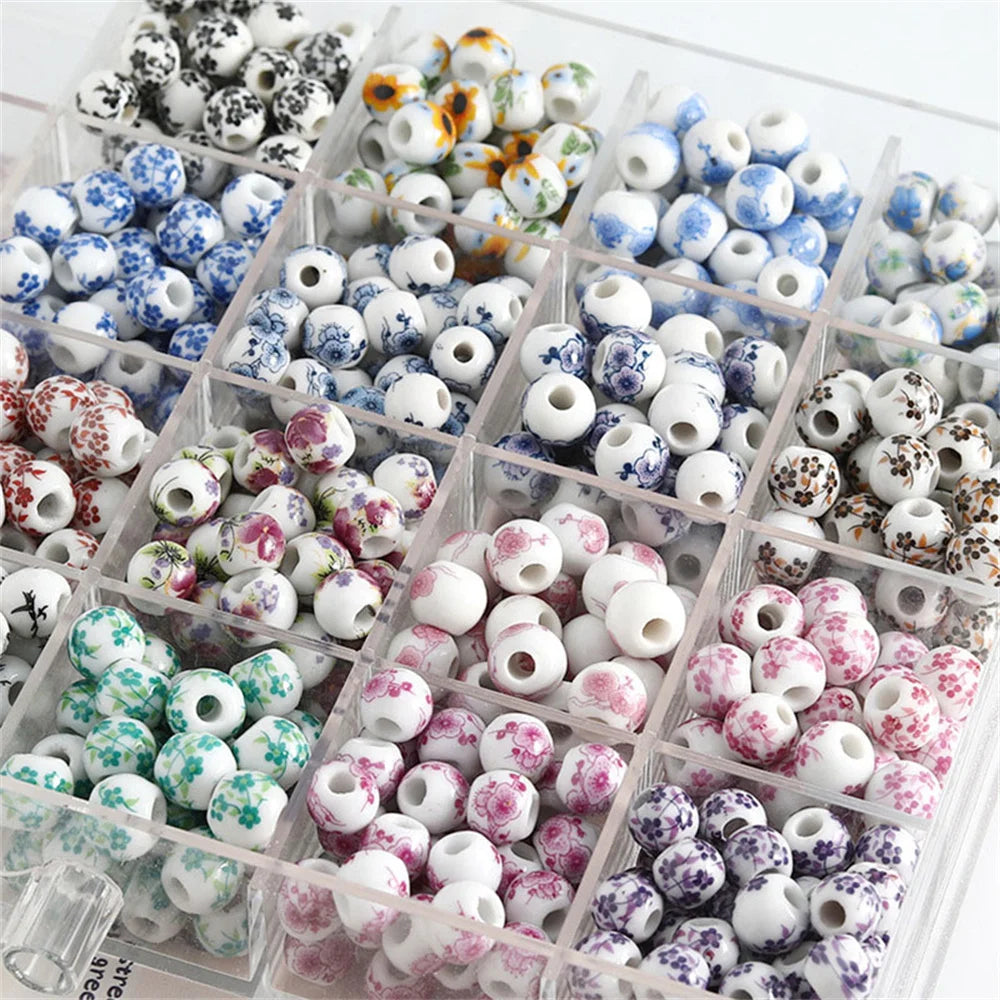A clear plastic container filled with small round ceramic flower beads in various blue, white, and pink colors for jewelry ma