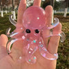 A hand holds a translucent pink stretchable octopus stress ball with glitter accents.