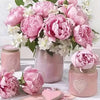 A bouquet of pink and white peonies and roses in a vase with paint by number kits nearby