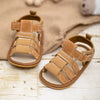A pair of tan soft non-slip baby sandals for first walkers resting on a light wooden surface.