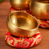 A golden Tibetan singing bowl resting on a red fabric surface.