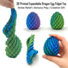 A hand holds a 3D printed expandable dragon egg fidget toy in various colors and shapes.