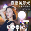 A woman is using a portable LED selfie ring light with a clip on a smartphone for lighting.