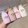 Three pink and white squishy milk bottles are held by a hand against a light background.