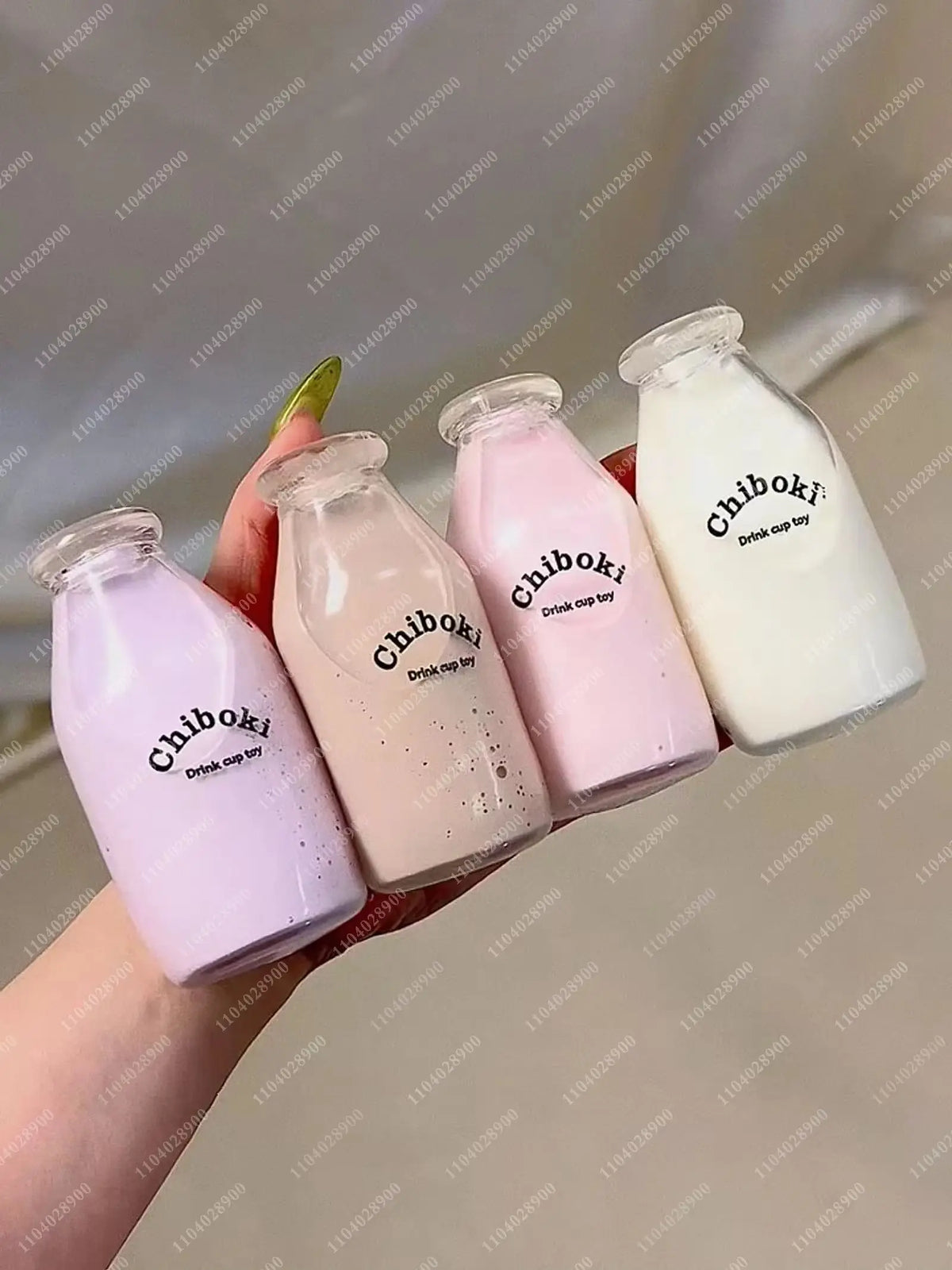 Three pink and white squishy milk bottles are held by a hand against a light background.
