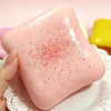 A pink squishy stress relief toy with red speckles is held above a white plate.