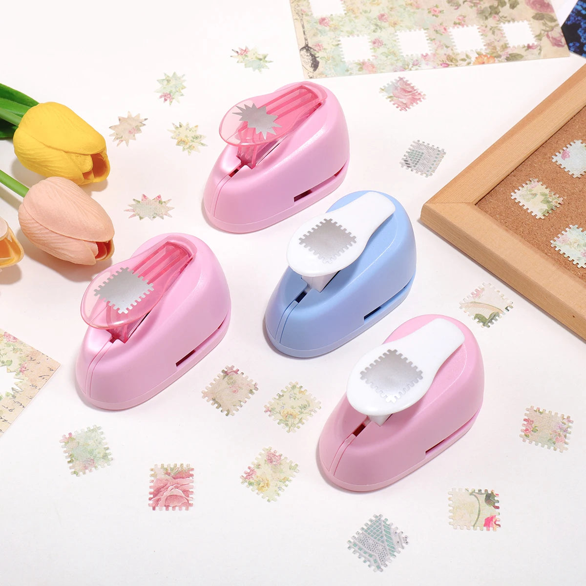 Three pink and blue lever action embossers for scrapbooking and card making placed on a white surface with floral stickers.