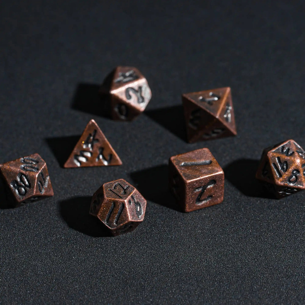 A collection of small, dark bronze metal dice and a triangular die are scattered on a dark surface.