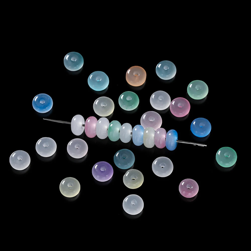 A collection of small, round glass spacer beads in various shades of green, blue, and pink are scattered on a black backgroun