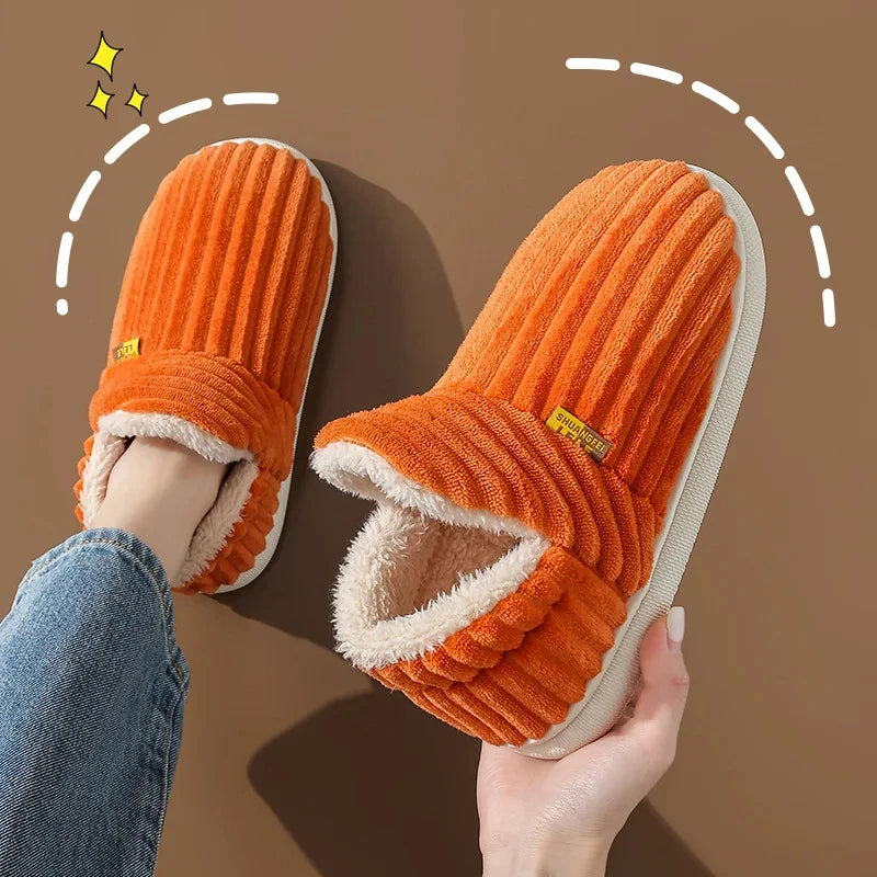A pair of bright orange faux fur slippers being held, showing the plush texture and indoor/outdoor design.