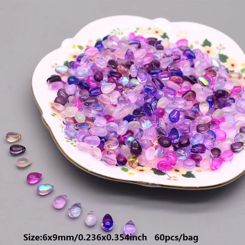 A pile of colorful water drop Czech glass beads in various shades of purple and pink on a white dish.
