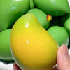 Eine Hand hält einen leuchtend gelben Mango-Form-Stressball neben grünen herumspielbaren Spielzeugen.