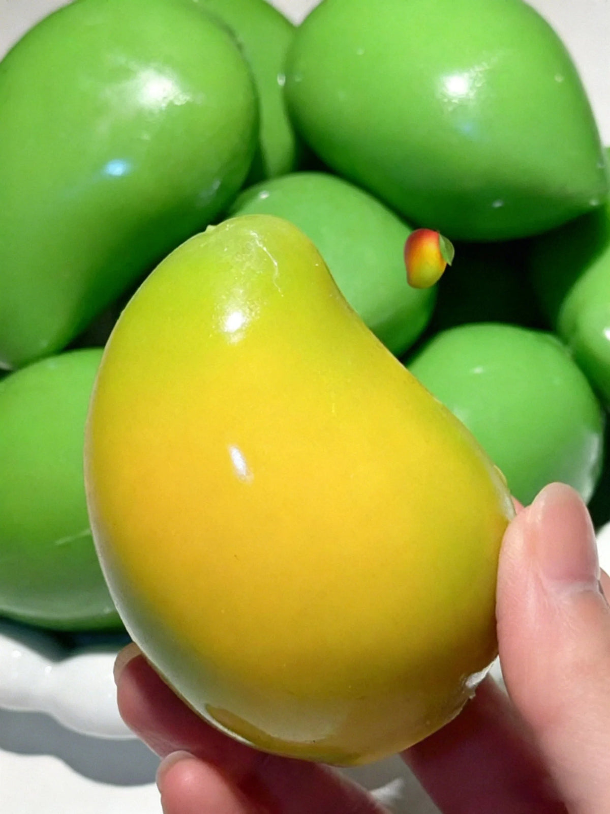Eine Hand hält einen leuchtend gelben Mango-Form-Stressball neben grünen herumspielbaren Spielzeugen.