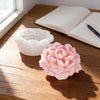 A pink peony flower silicone mold resting on a wooden table next to an open notebook.