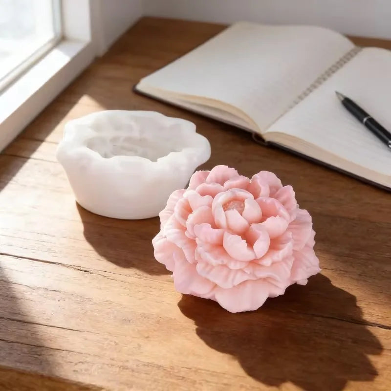 A pink peony flower silicone mold resting on a wooden table next to an open notebook.