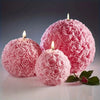 Pink rose flower ball silicone mold with lit candles on a white surface
