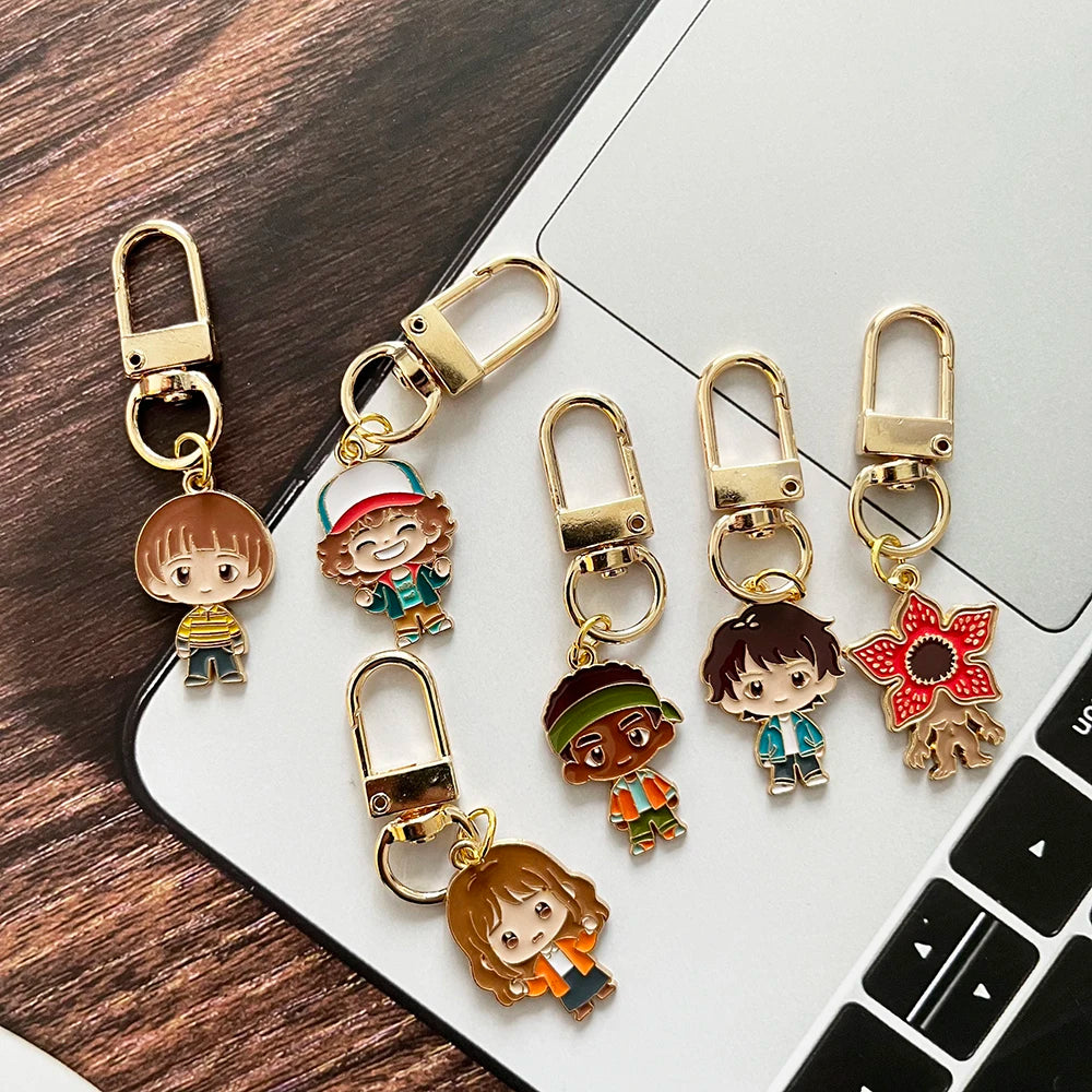 A set of six metal keychains featuring character pendants from Stranger Things, including a doll and various characters.