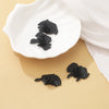 A set of black dragon dice enamel pins displayed on a white ceramic dish.