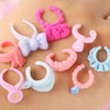 A collection of ten colorful plastic mini pet collar accessories in various shapes and colors laid out on skin.