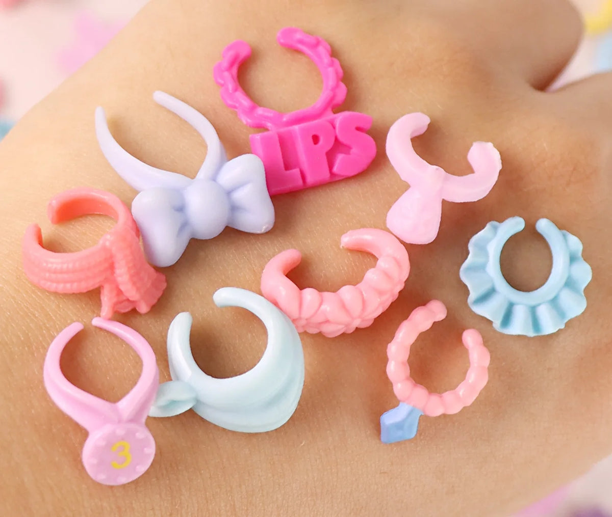 A collection of ten colorful plastic mini pet collar accessories in various shapes and colors laid out on skin.