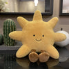 A yellow sun plush toy with a smiling face is displayed on a reflective surface next to a green cactus and a white spherical 
