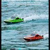 A person holds a black remote control, operating a green high-speed boat on the water.