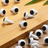 A collection of white plastic safety eyes with black pupils arranged on a wooden surface.
