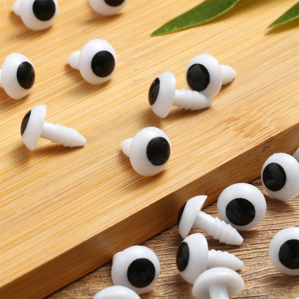 A collection of white plastic safety eyes with black pupils arranged on a wooden surface.
