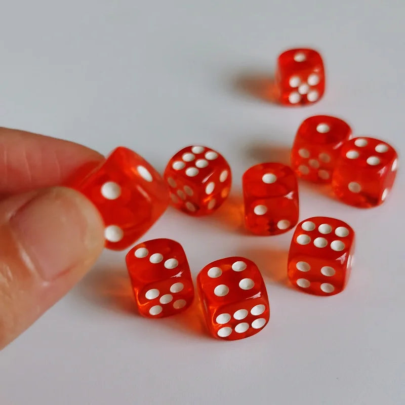 A hand holds several small, transparent red dice with white dots on a white surface.