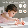 A baby is exercising their hands on a pink silicone toy car while learning fine motor skills and cognitive ability.
