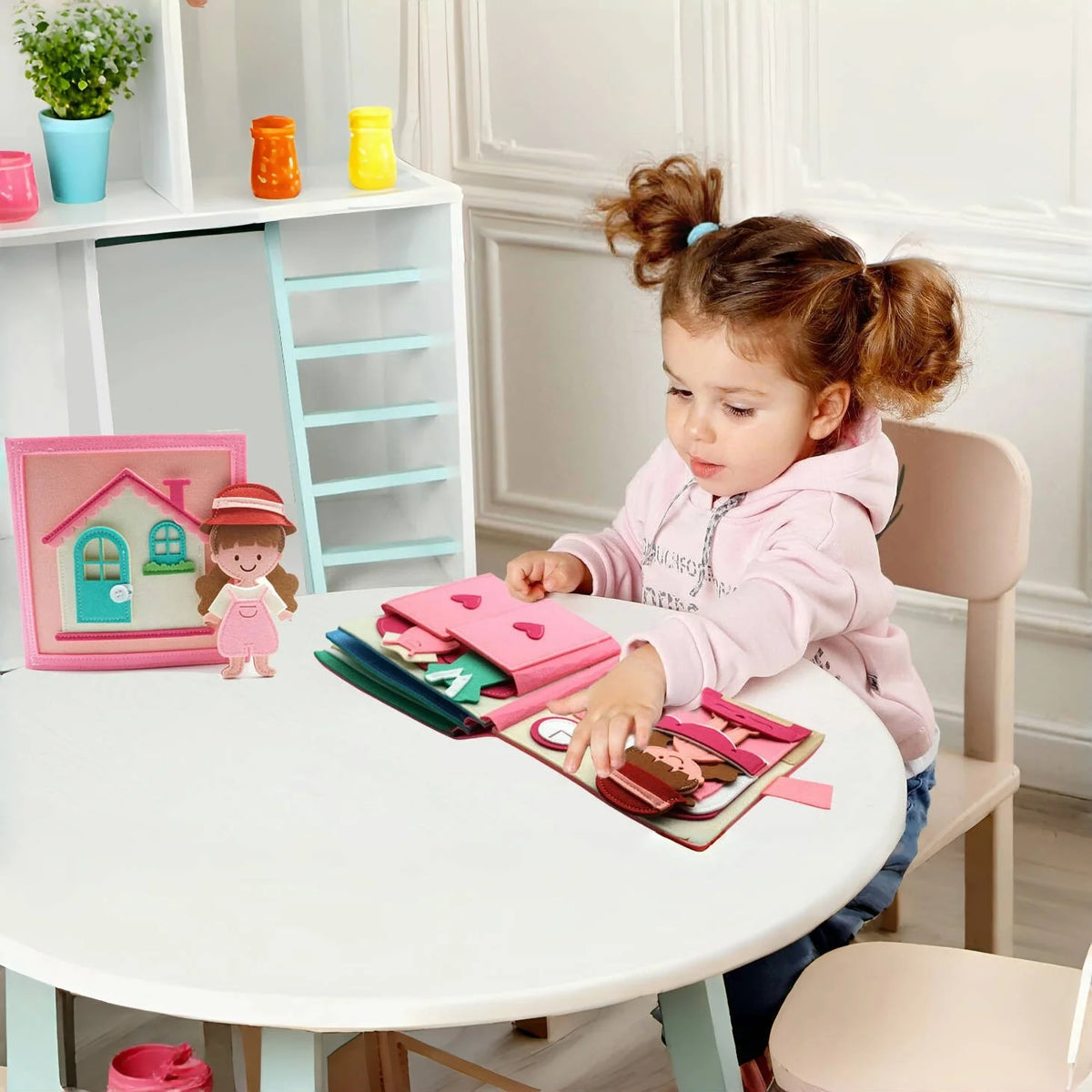 A young girl is interacting with a pink felt busy book on a white table in a brightly lit room.
