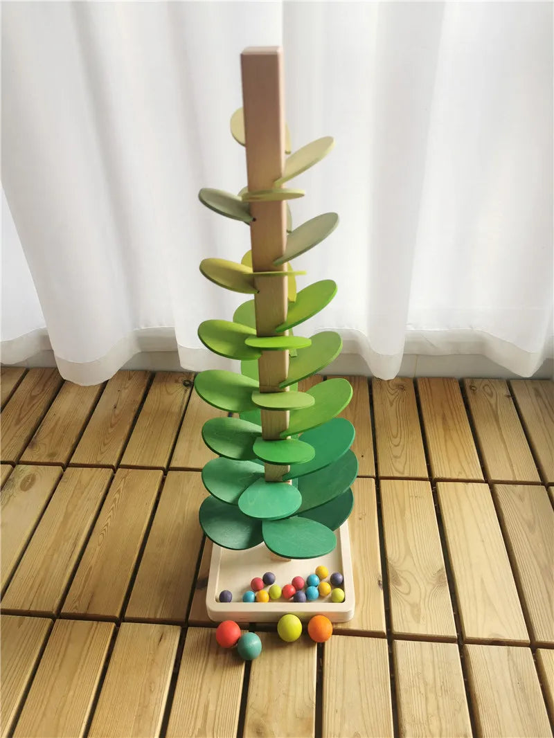 A wooden sensory music tree structure with green leaves and a marble run is displayed on a light wooden floor.