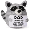 A gray crochet plush toy shaped like a raccoon with black markings, featuring a tag that reads Dad thanks for loving me even 