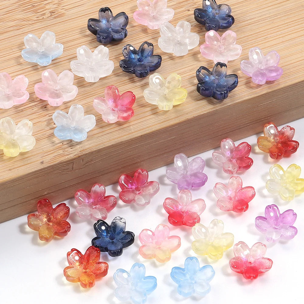 A collection of 50 glass cherry blossom flower beads in various pastel and deep blue colors arranged on a wooden surface.
