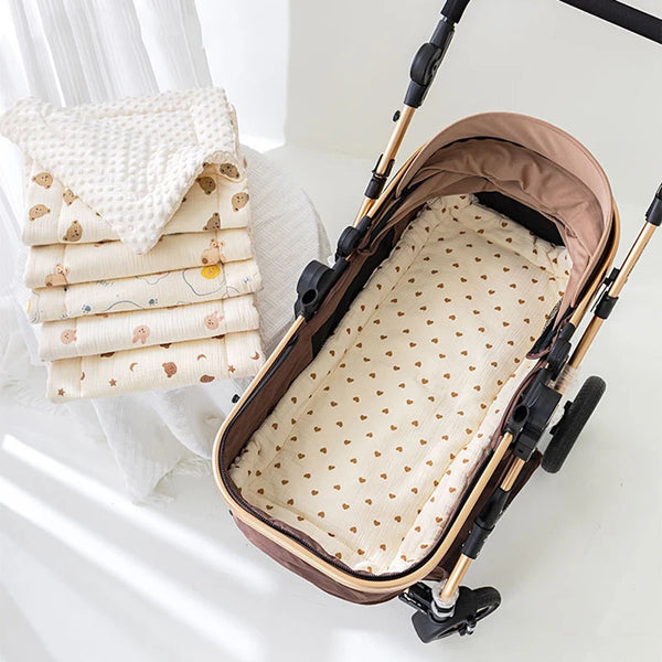 A brown soft cotton mattress is shown inside a baby stroller, next to a stack of white patterned cloths.
