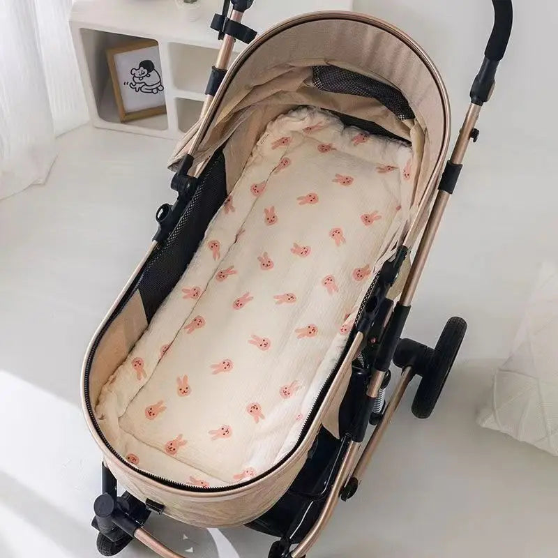 Matelas en coton doux beige pour poussette de bébé sur une surface blanche.