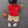 A red polo shirt and beige shorts set for a boy, with a small wooden animal charm nearby.