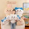 A woman is sitting on a couch surrounded by several Chiikawa plush dolls, including Hachiware and Usagi.