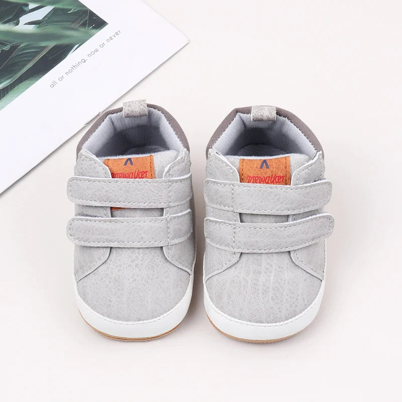 A pair of gray baby first walker shoes with suede fabric and anti-slip TPR soles are shown next to a white card.
