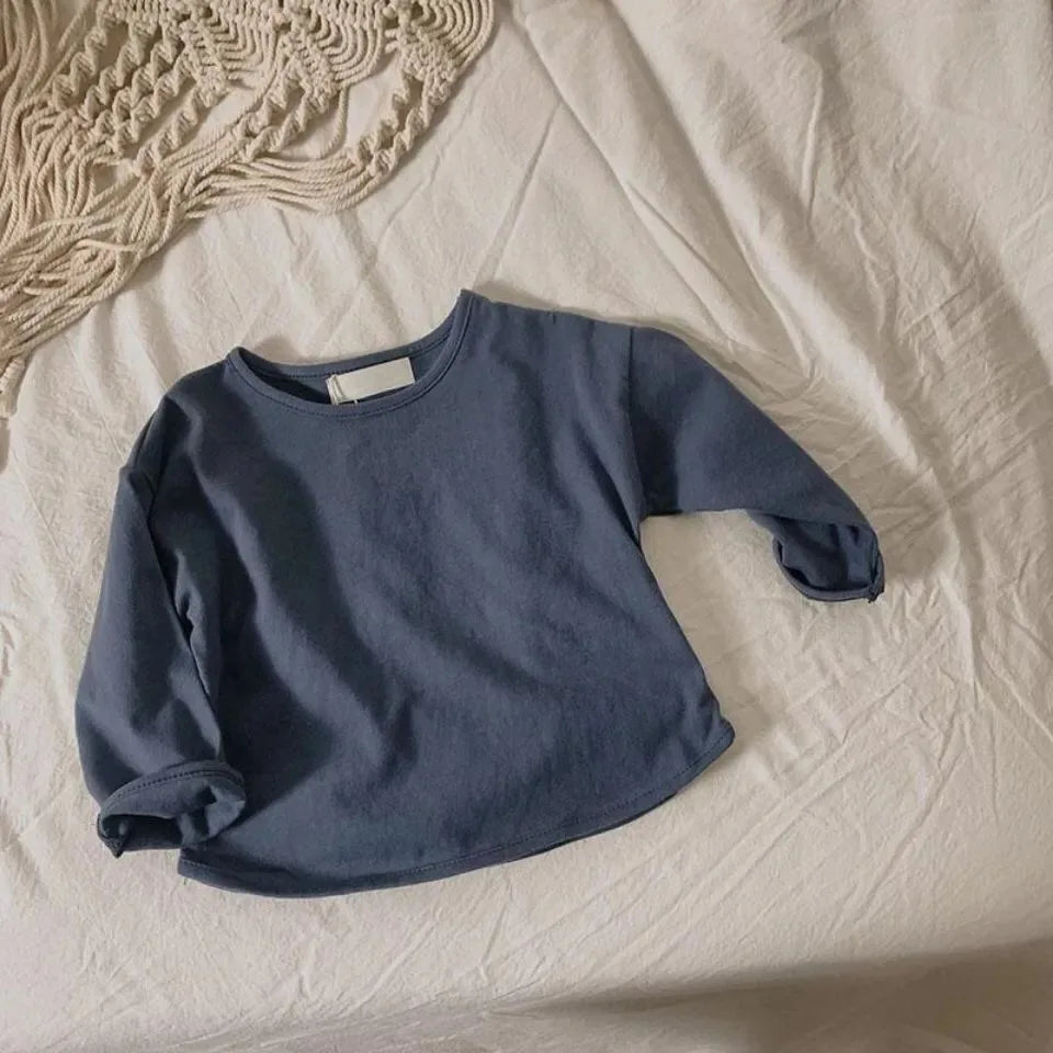A navy blue kids long sleeve cotton tee laid flat on a white sheet.