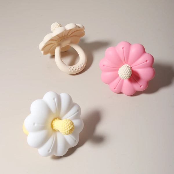 Three silicone teethers shaped like flowers in white, pink, and white with yellow accents.