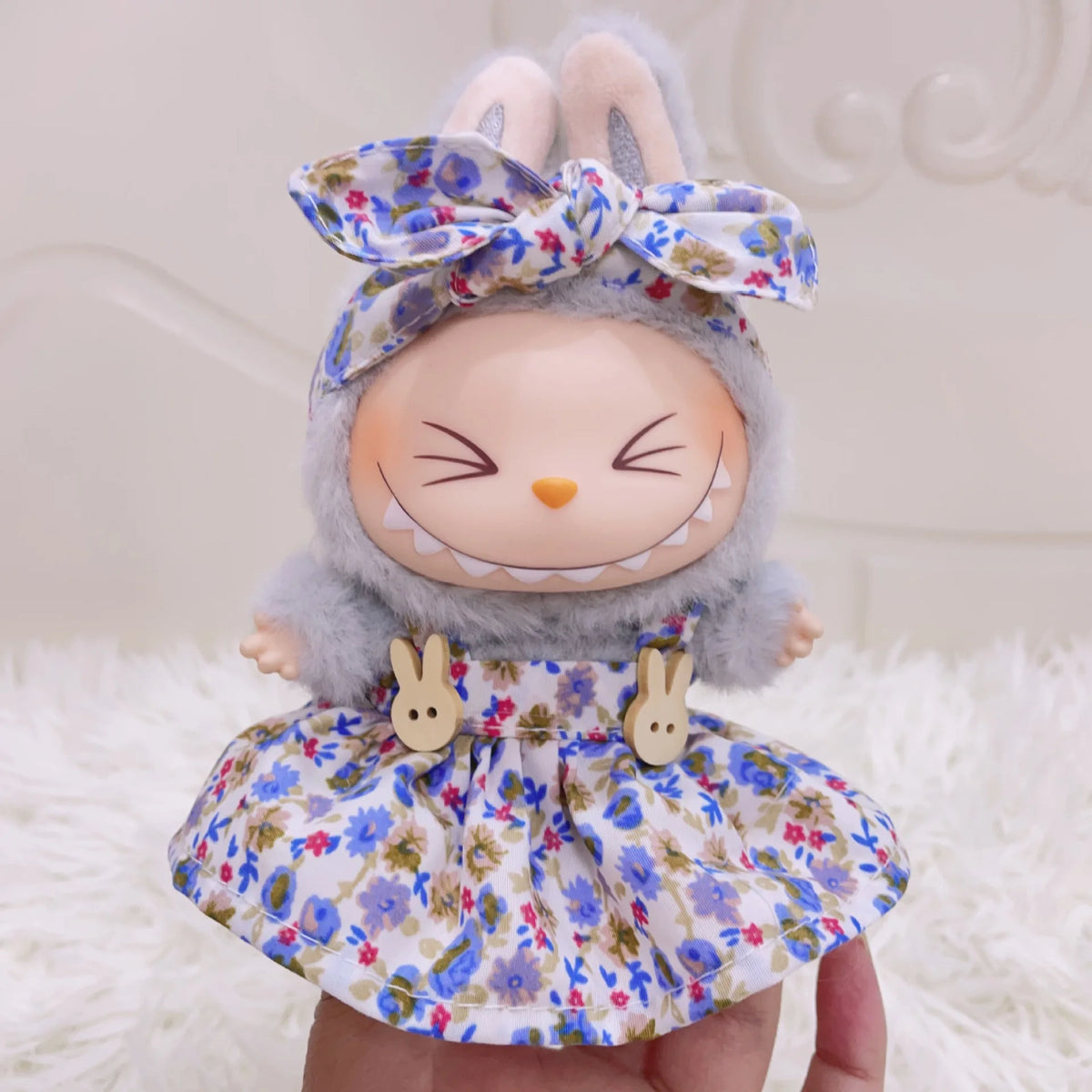 A cute rabbit-themed doll wearing a floral dress and bow, displayed on a white fluffy surface.
