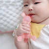 A baby is holding a pink silicone teether toy with a nipple on their lips.