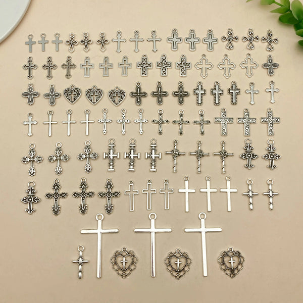 A collection of vintage silver cross charms and pendants for jewelry making displayed on a light background.